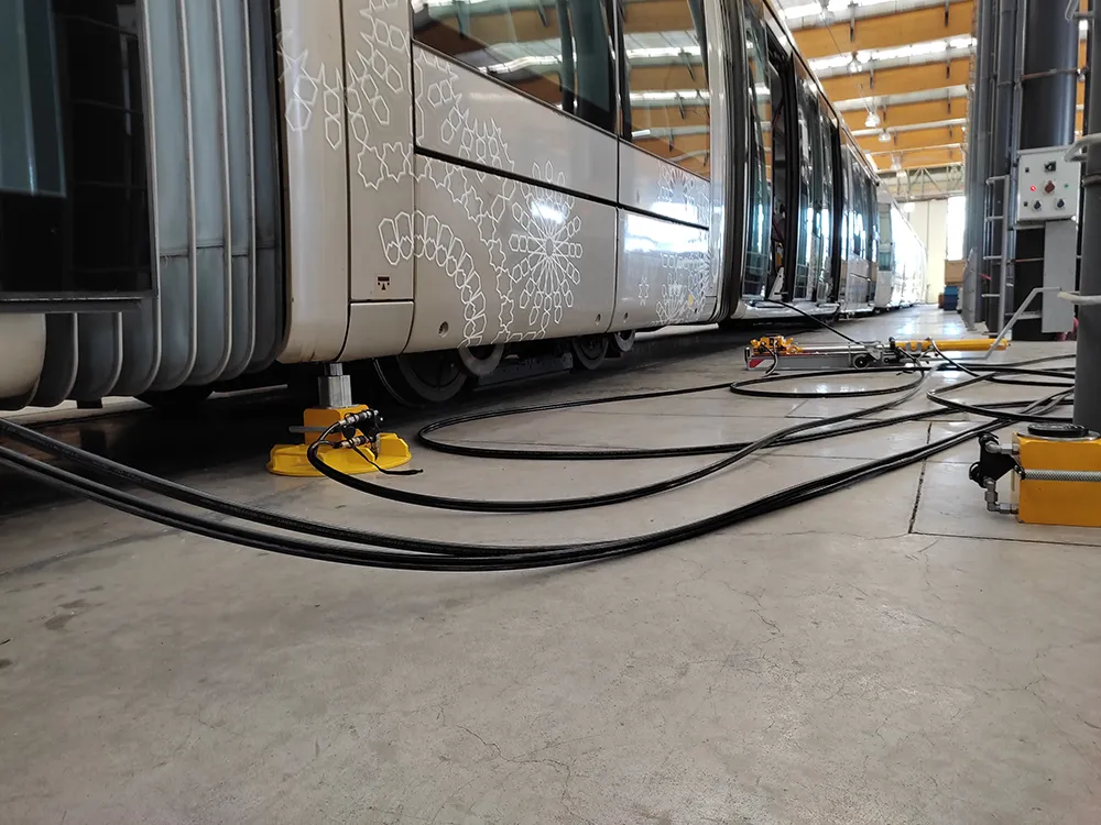 Vérins de levage hydraulique et câbles installés sous une rame de tramway en atelier pour la maintenance ferroviaire