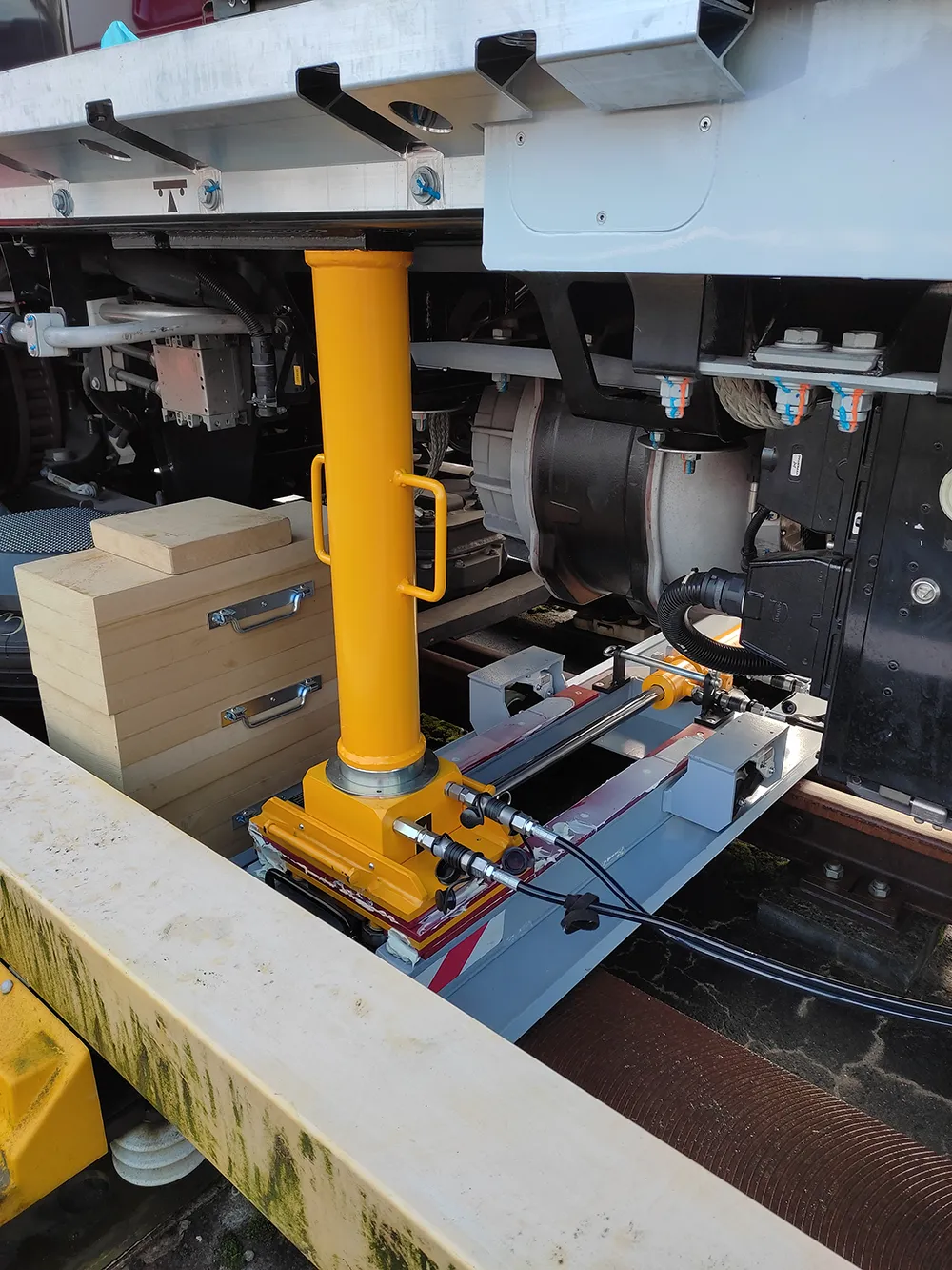 Vérin hydraulique de levage jaune déployé sous le châssis d'un train pour une opération de maintenance ferroviaire